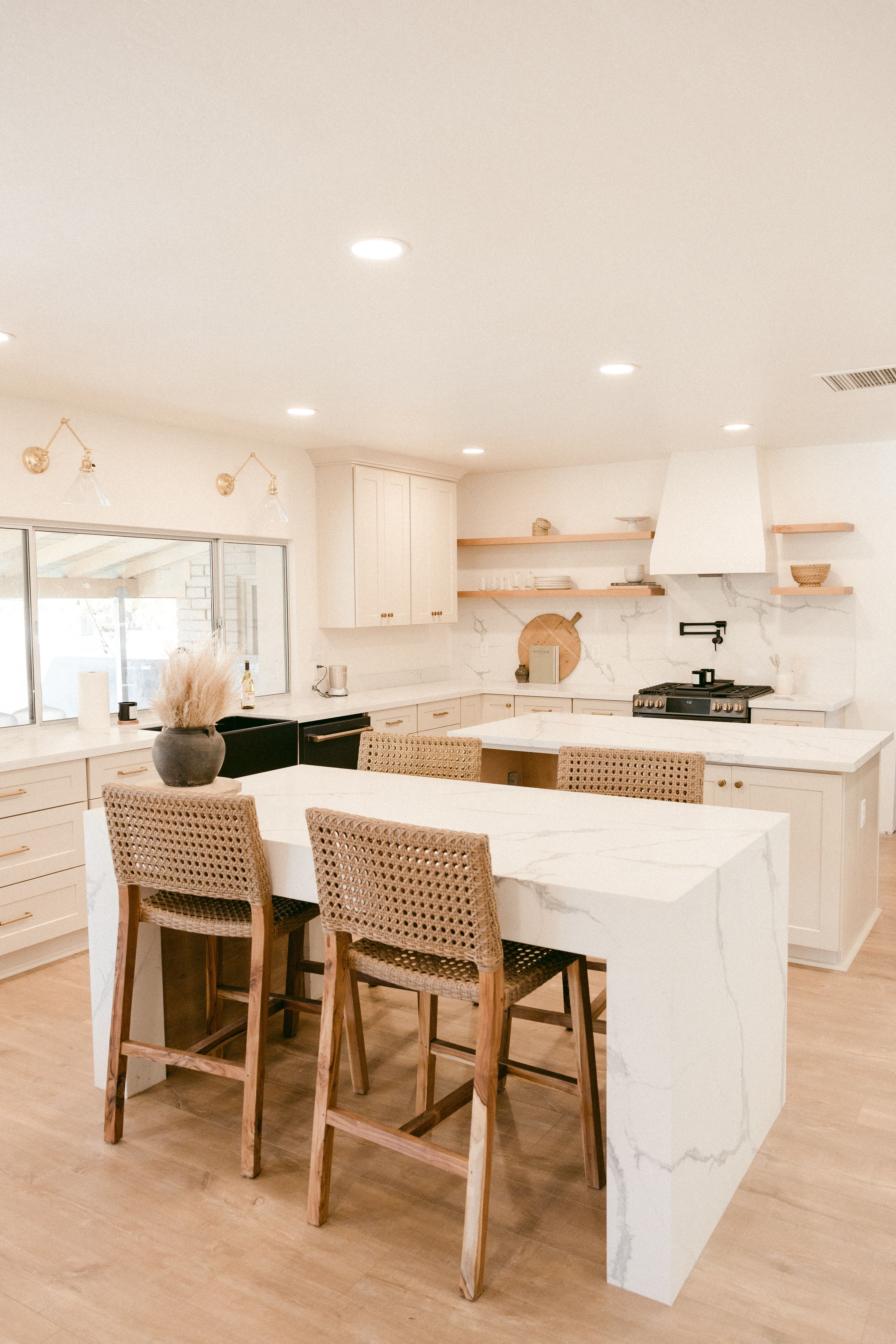 Bright kitchen with a large marble island, woven bar stools, and brass fixtures.