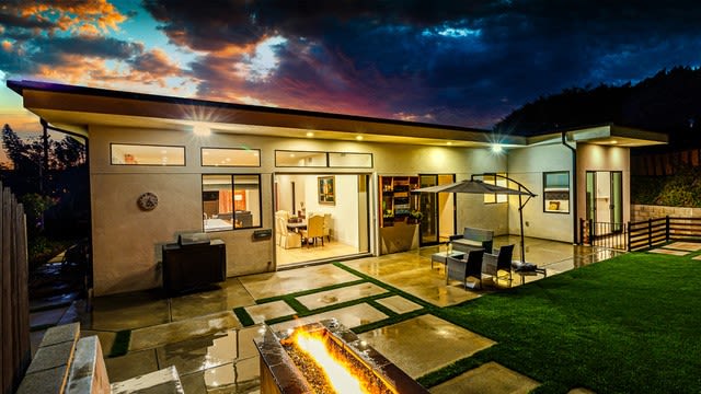 Modern Solana Beach home at dusk with a glass-walled patio, fire feature, and lawn.