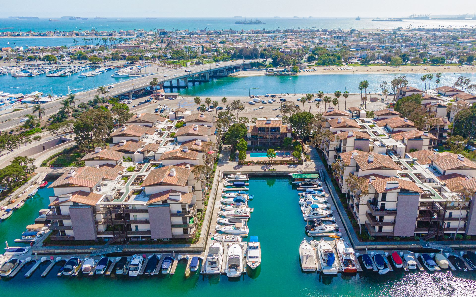Aerial view of marina-side condominiums, boat slips, a bridge, and coastal waterways.