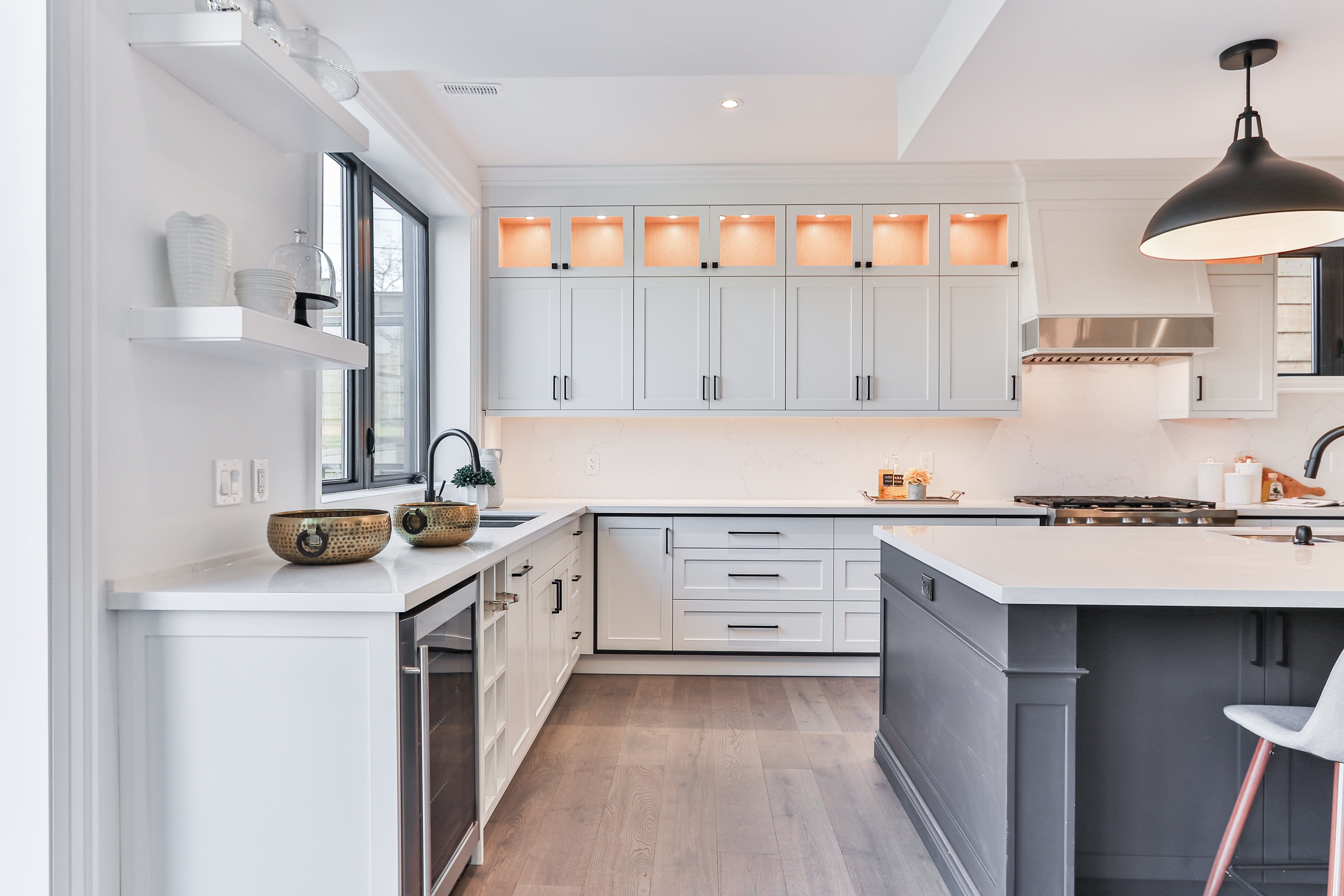 Modern kitchen with white cabinetry, lit display niches, and a large charcoal-gray island.