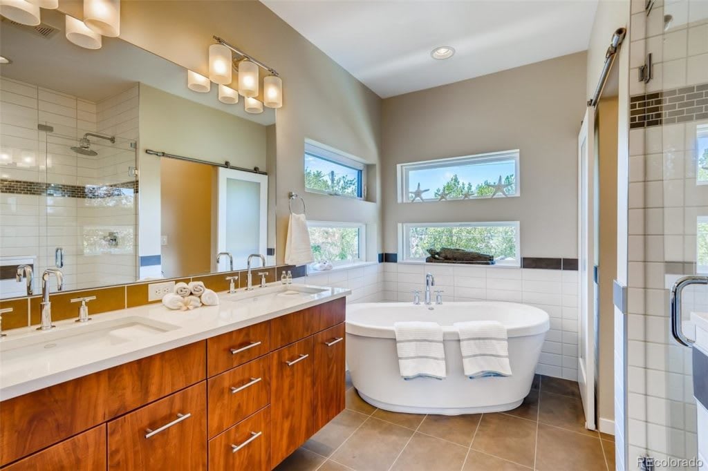 Bathroom with a freestanding soaking tub, double vanity, and high windows.