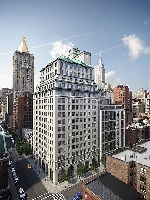 Light-colored city building with a green roof, seen from above among surrounding buildings.