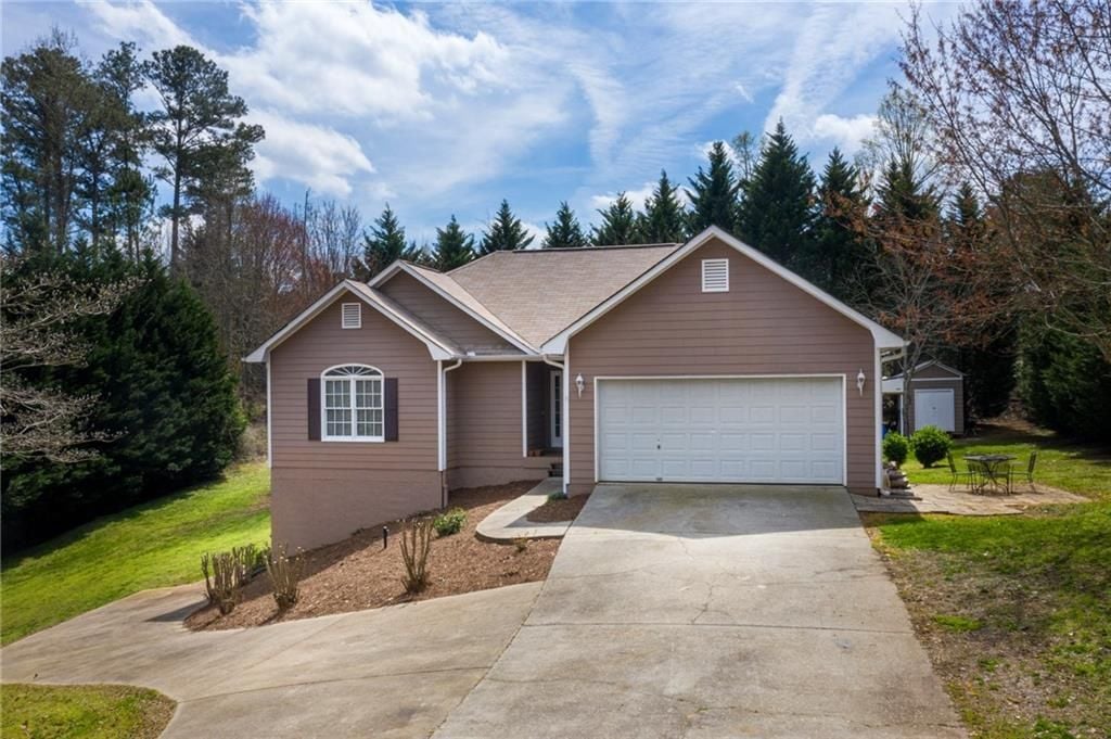 Brown single-story home with a two-car garage, wide driveway, and mature trees.