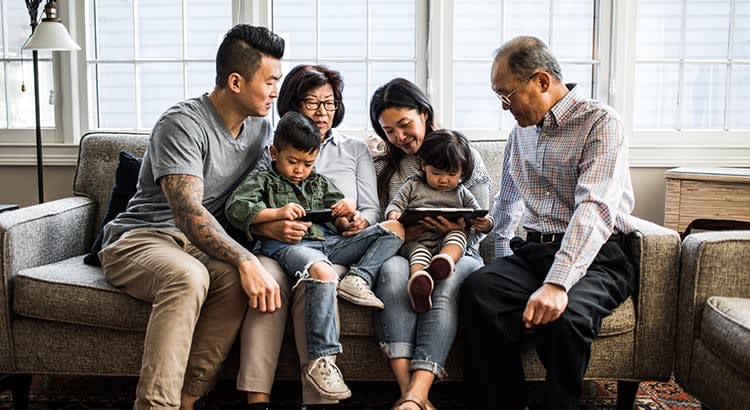 A multi-generational family sitting together on a couch. There are two adults, two elderly individuals, and two young children.