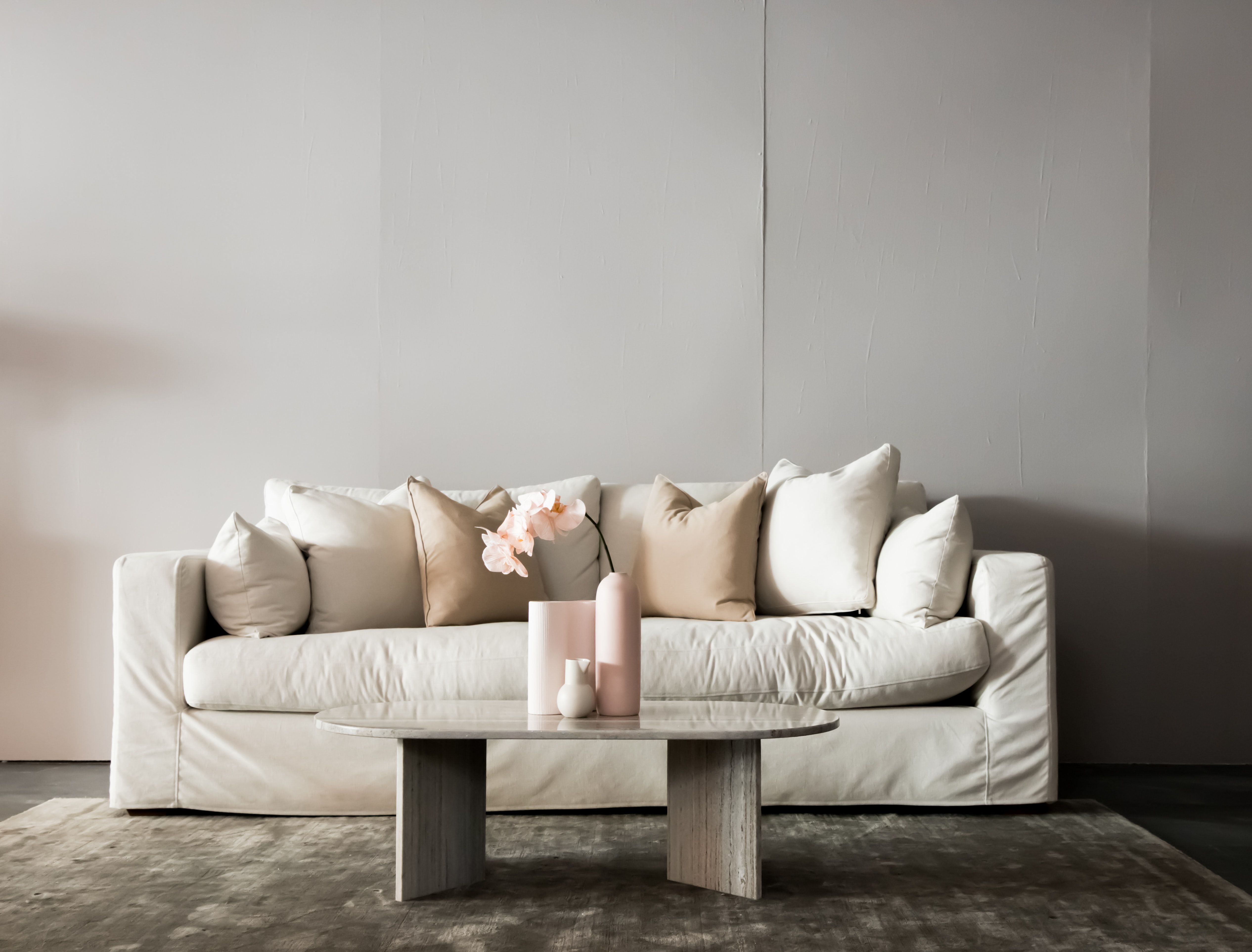 White living room sofa with neutral cushions and pale pink flowers on a low coffee table.