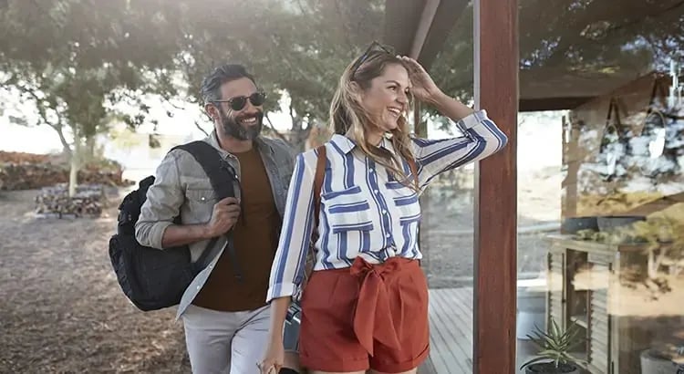 A happy couple with backpacks, walking outdoors in a casual setting, suggesting travel or an enjoyable outing.