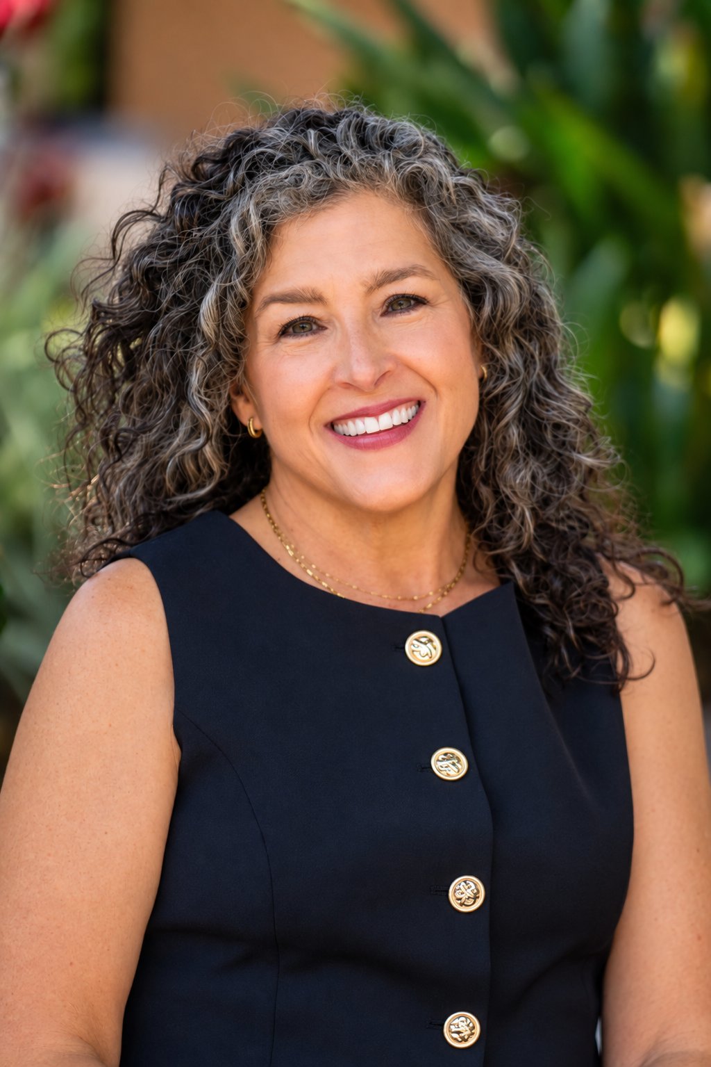 Jonna Lewis smiling outdoors in a navy dress, with long curly salt-and-pepper hair.