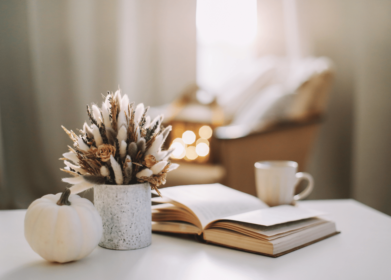 Autumn table decor with a white pumpkin, dried flowers, an open book, and a mug.