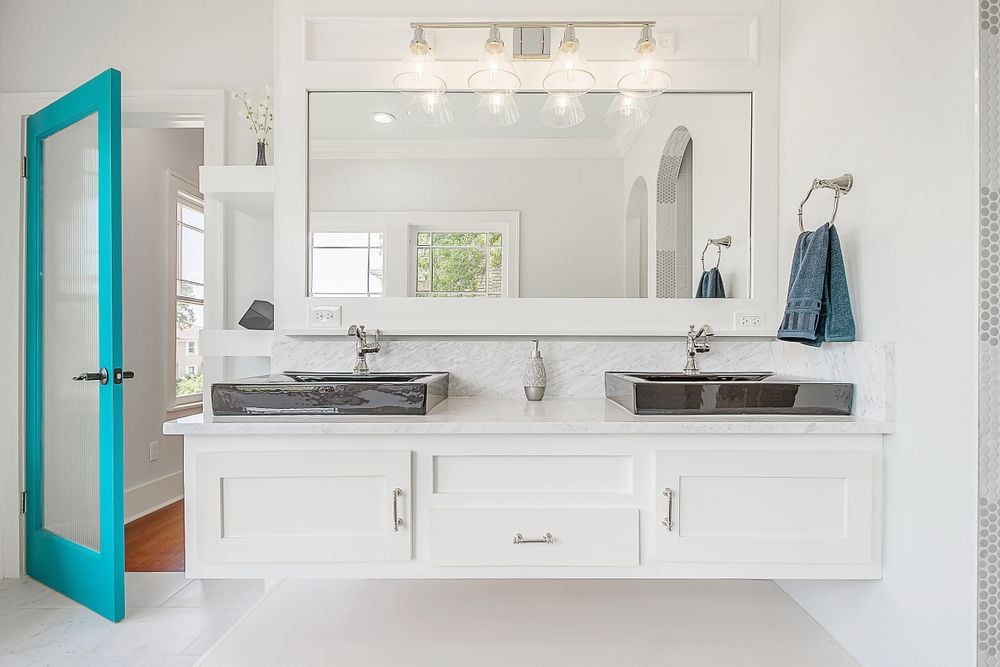 Bright white bathroom with a double vanity, dark vessel sinks, and an open turquoise door.