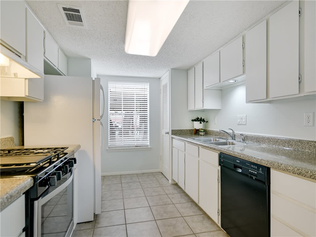 Galley kitchen with white cabinets, a gas range, and a sink beneath granite-look counters.