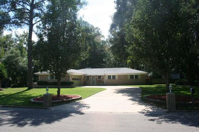 A long driveway leading to a house surrounded by trees and a well-maintained lawn.