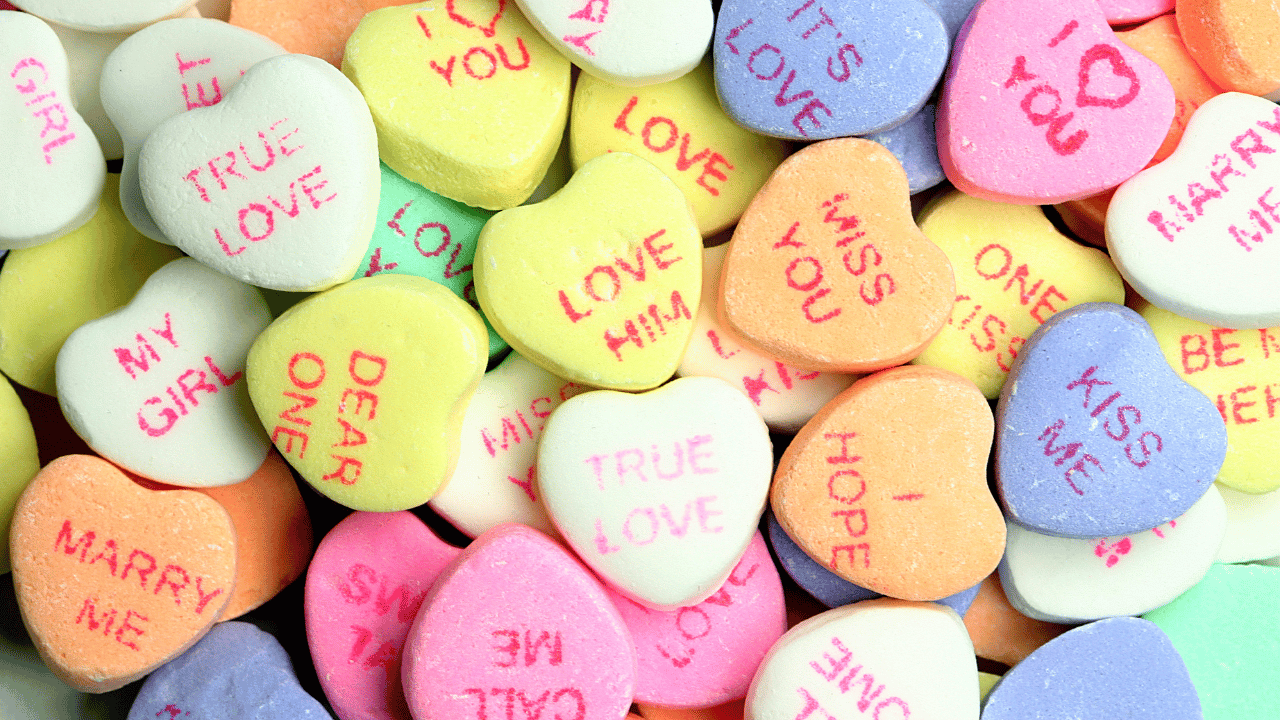 A collection of colorful heart-shaped candies, typically associated with Valentine's Day. Each candy has a short, affectionate message printed in pink text.