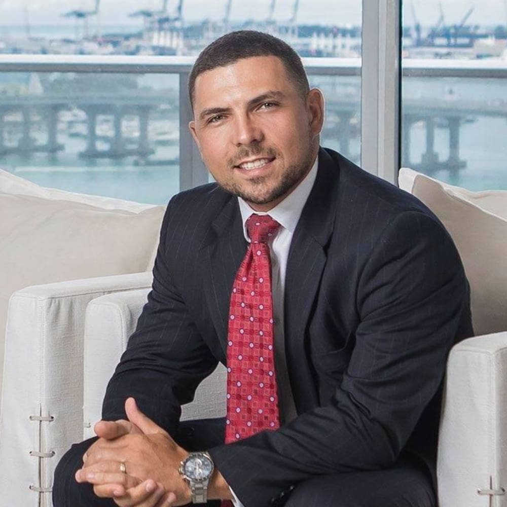 Michal Bander, a real estate professional in a suit and tie, seated on a couch.