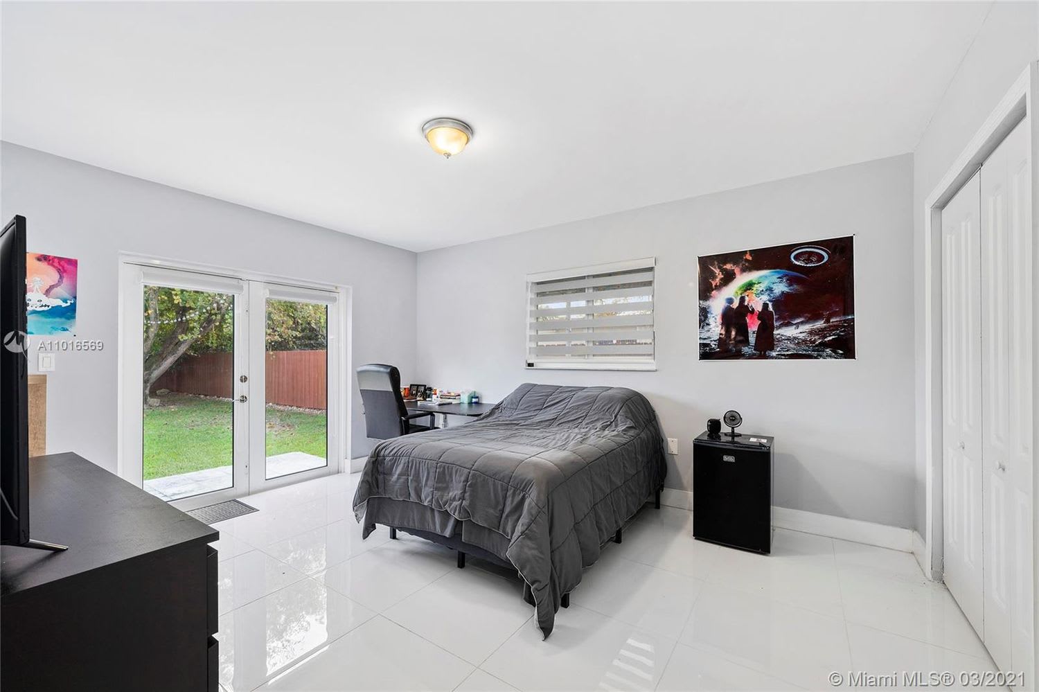 Bedroom with a gray bed, white tile floors, and sliding glass doors opening to the backyard.