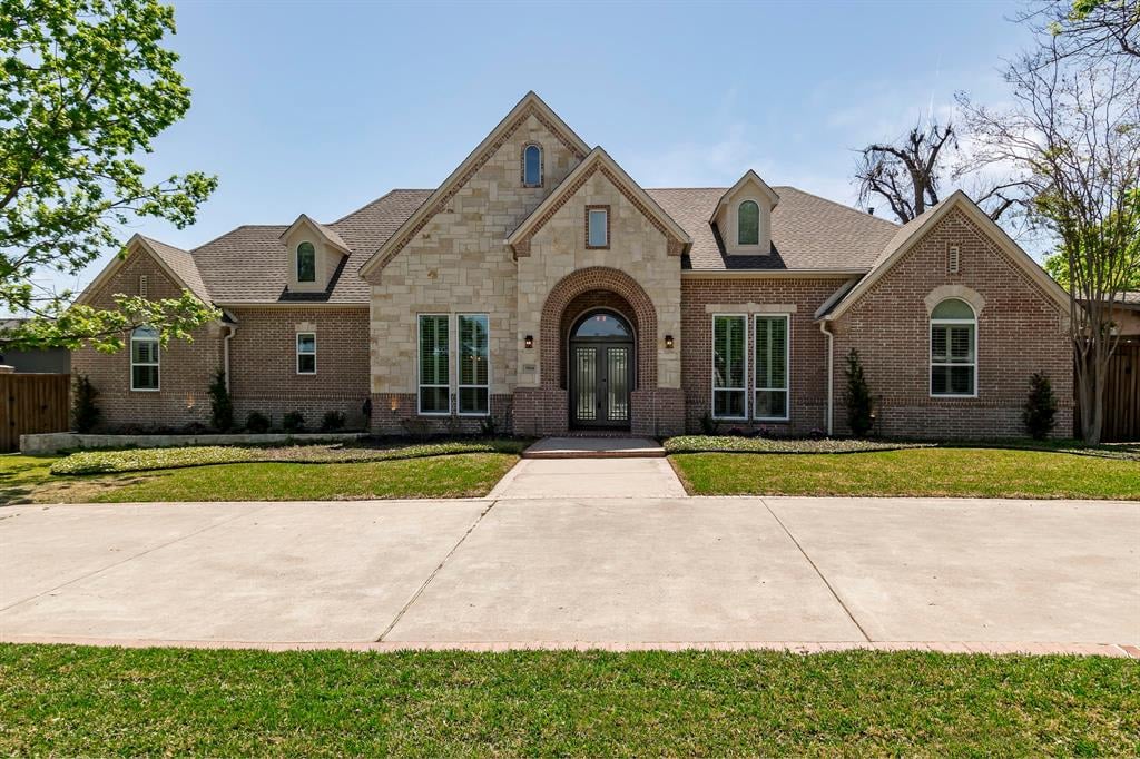 Brick and stone home with a tall arched entry, front lawn, and wide driveway.