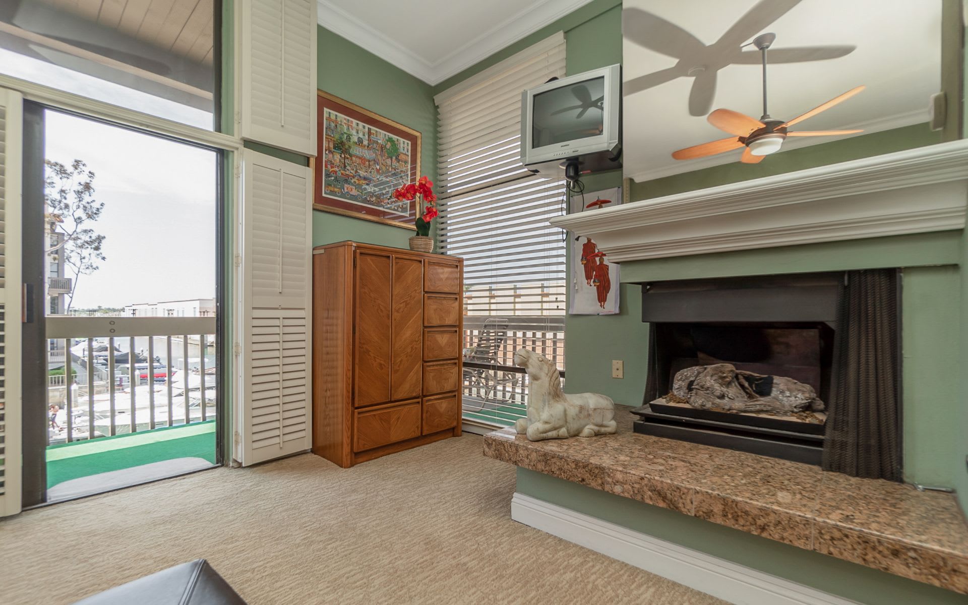 Living room with a stone fireplace, sage-green walls, and a sliding glass door to a marina-view balcony.