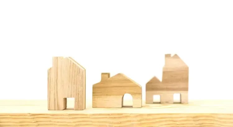 A minimalist image featuring small wooden house models on a light background.