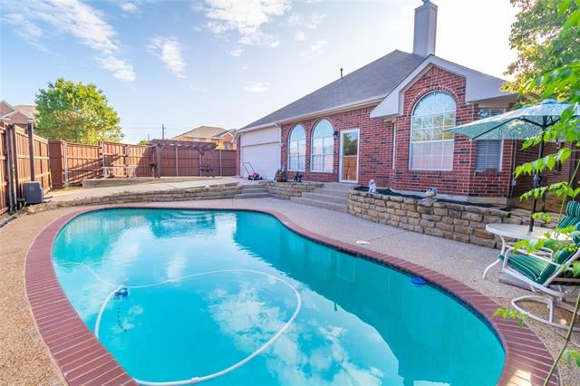 Backyard swimming pool beside a red brick house, with a curved shape and fenced patio.