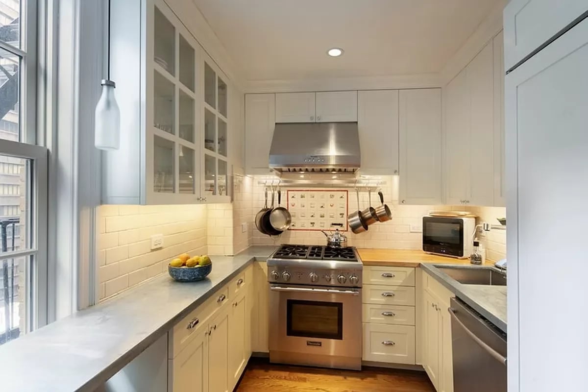 Kitchen with white cabinets, stainless steel range, pale counters, and large windows.