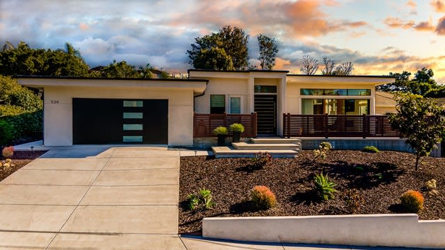Modern single-story home with a broad driveway, landscaped front yard, and warm sunset light.