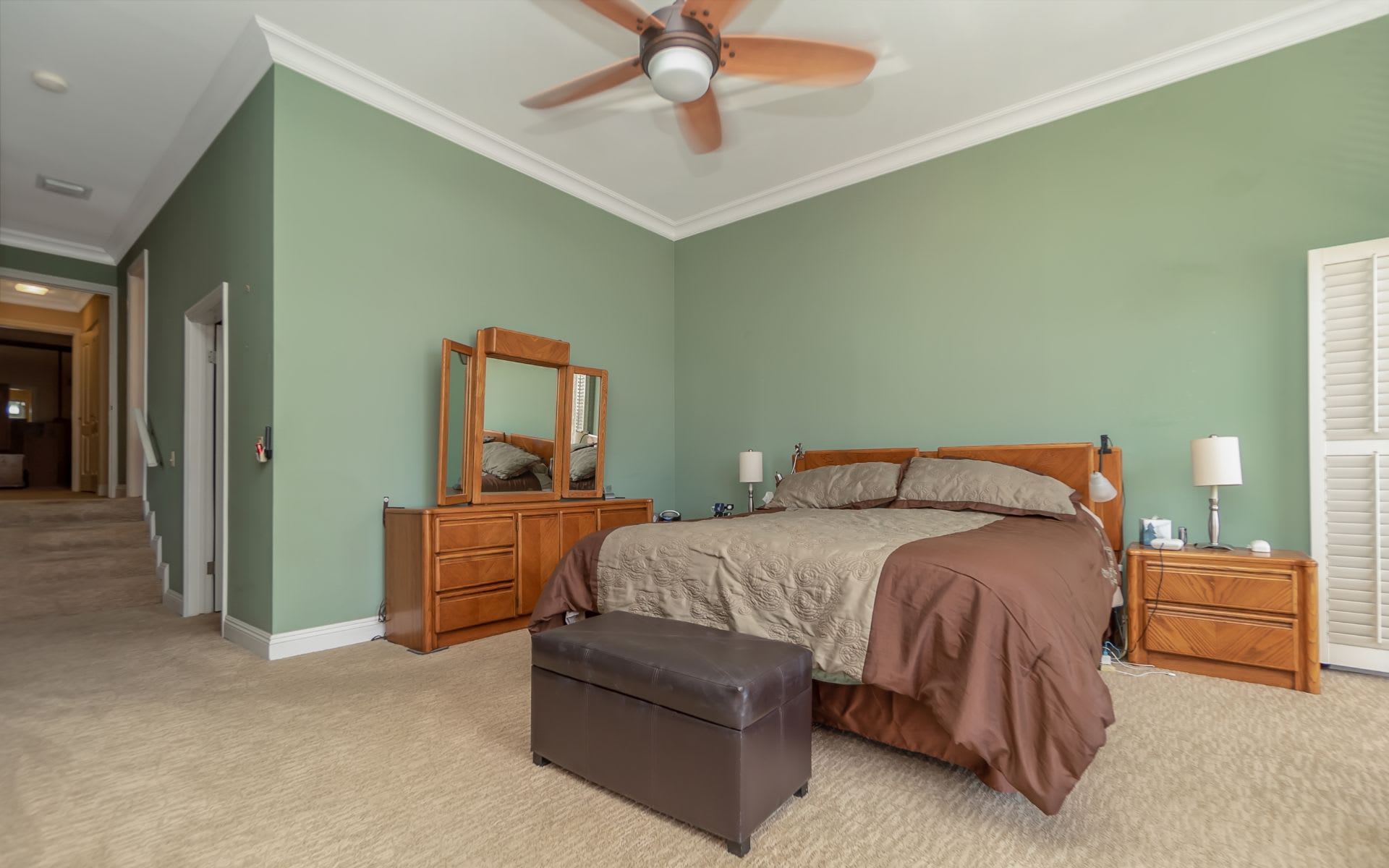 Furnished bedroom with a king-size bed, sage-green walls, wooden furniture, and a ceiling fan.