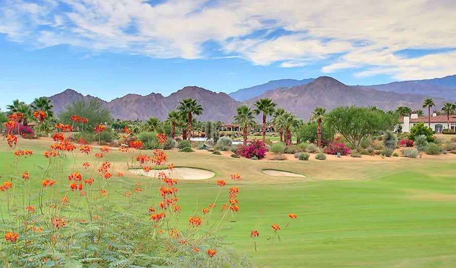 A lush green golf course with a sand trap in the foreground.