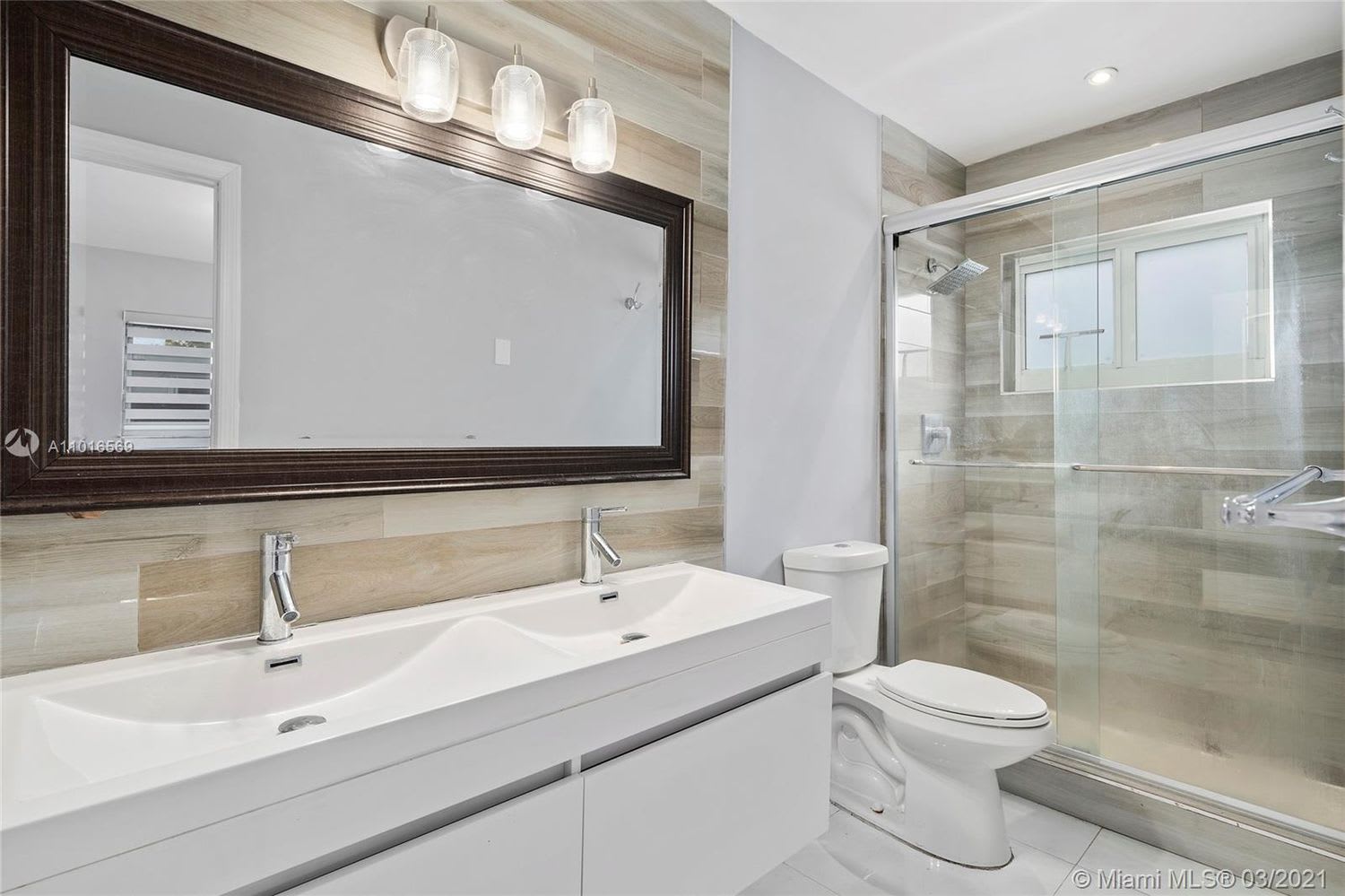 Bathroom with a double-sink vanity and glass-enclosed shower beneath a high window.