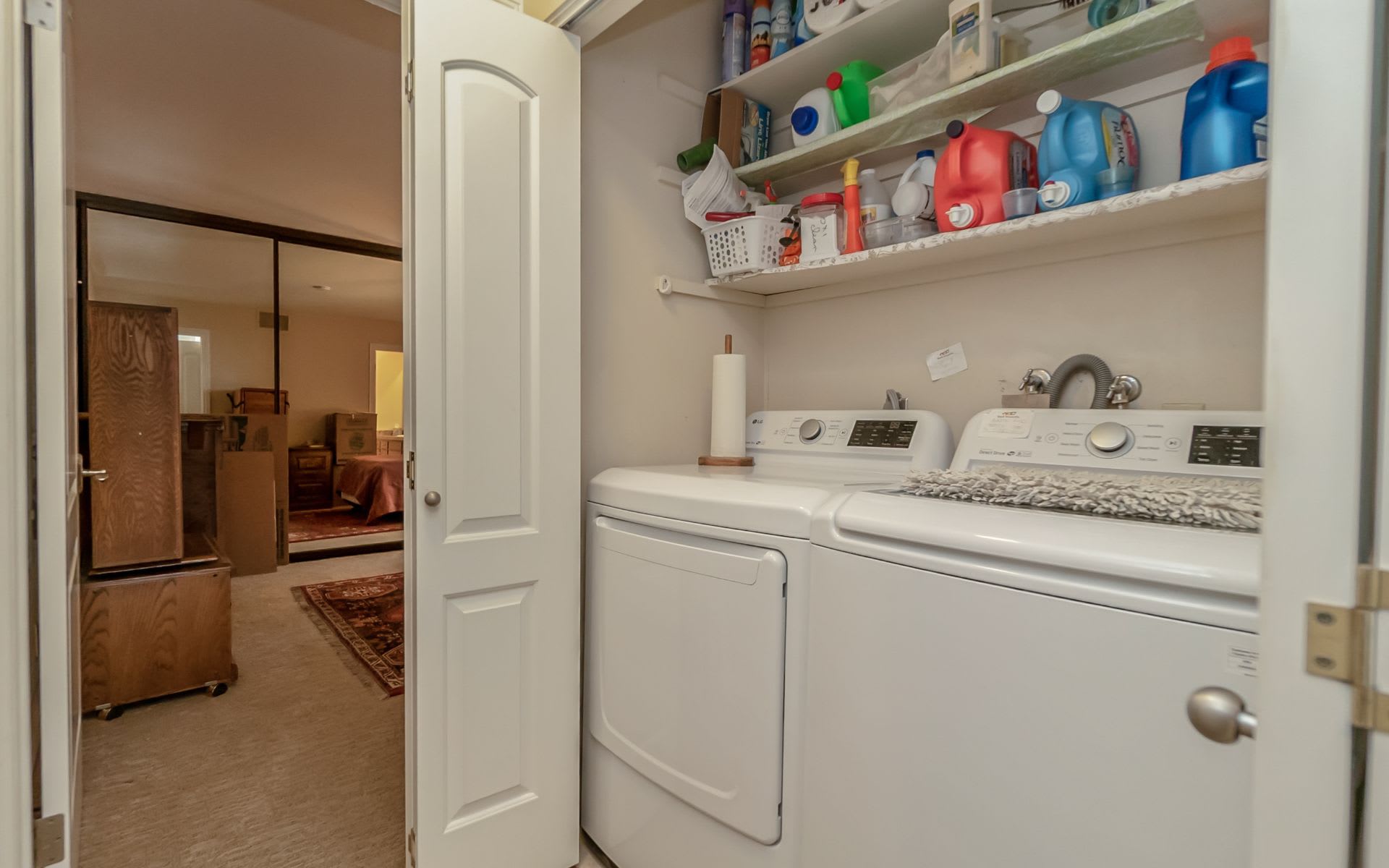Laundry room with white washer and dryer beneath shelves stocked with supplies.