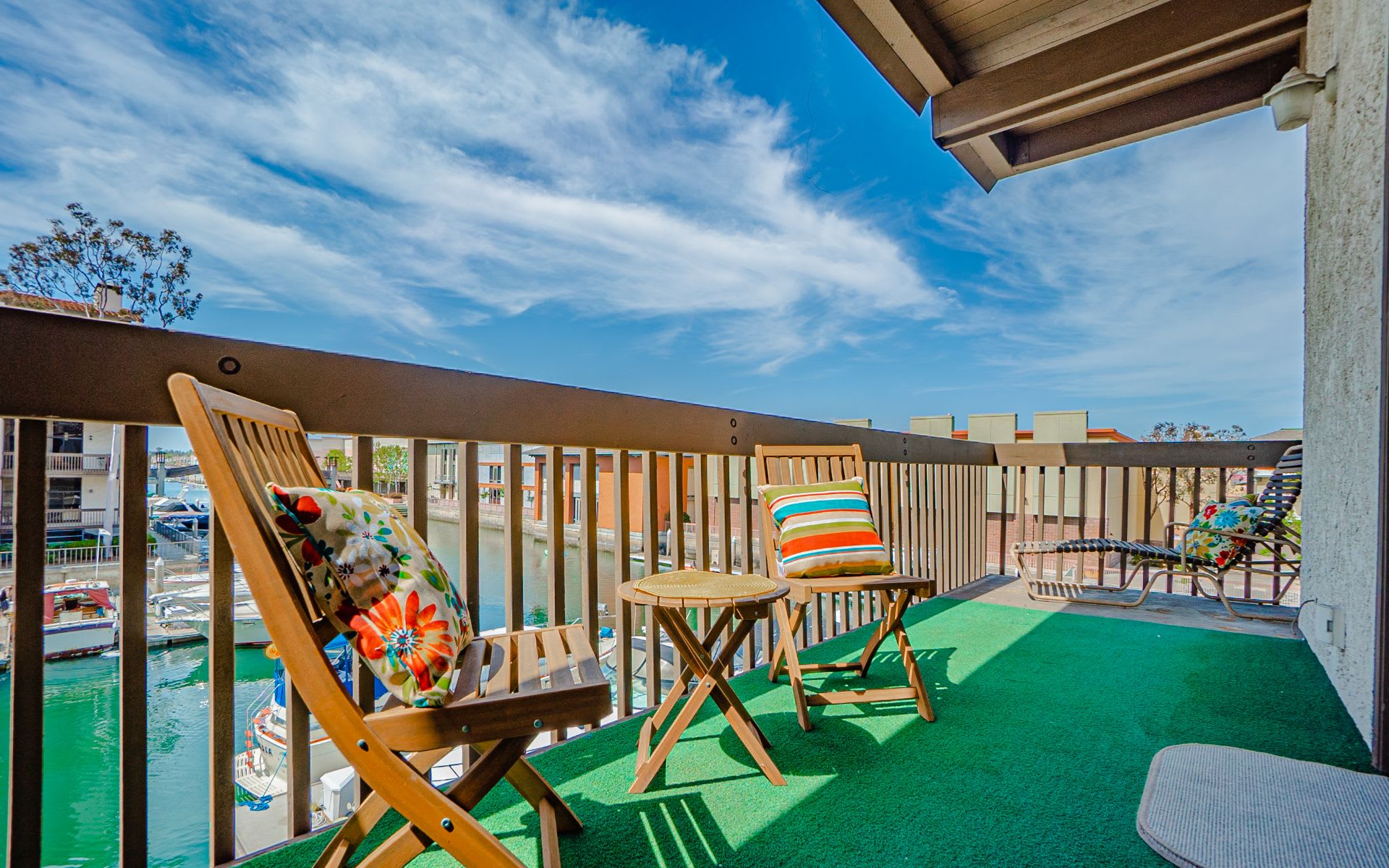 Waterfront balcony with wooden deck chairs overlooking marina water and boats.