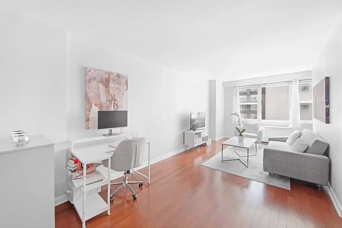 Bright living room with gray sofa, large windows, and a desk in the foreground.