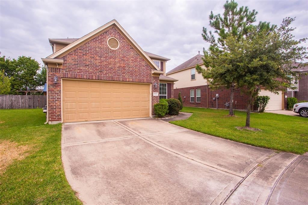 Two-story brick house with a tan double garage door, wide driveway, and mature trees.