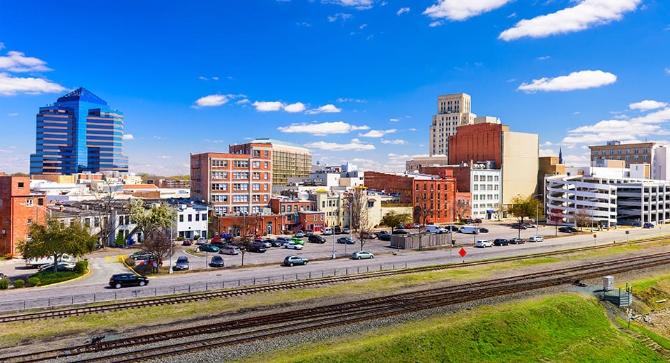 The Durham skyline with a mix of notable buildings of various heights and styles, and train tracks in the foreground.