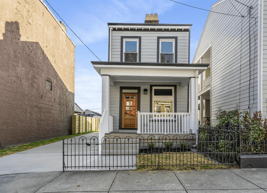 A small house with a porch and a wrought iron fence in front of it.