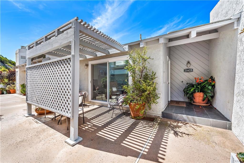 Home entrance with a slatted pergola, lattice screen, patio chairs, and potted plants.