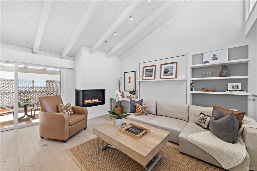 Staged living room with a vaulted beam ceiling, lit fireplace, and sliding doors to a lattice-enclosed patio.