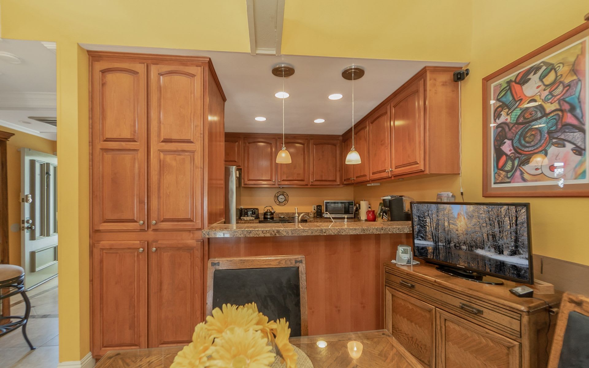 Kitchen with warm wood cabinetry, granite breakfast bar, and colorful framed artwork.
