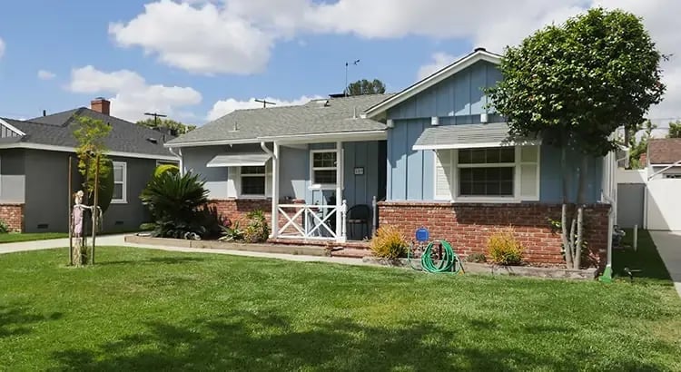 A suburban house with a neatly trimmed lawn and landscaping. This house has a blue exterior with white trim and a porch.