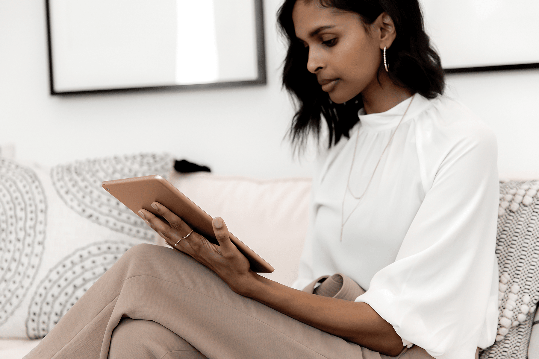 Woman in a white blouse seated on a patterned sofa, using a tablet.