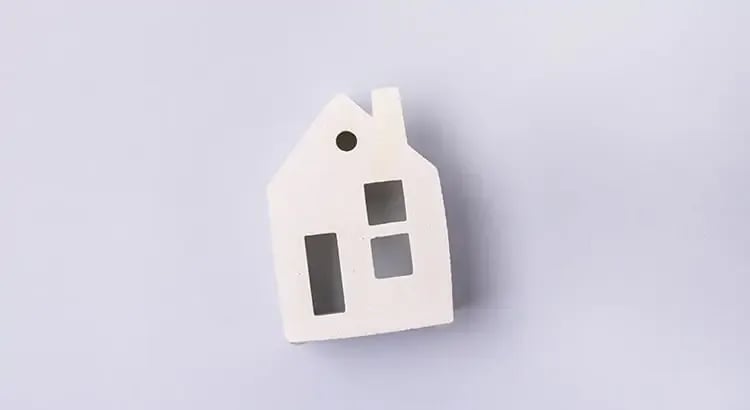 A small white house model against a light background, symbolizing real estate or home ownership.