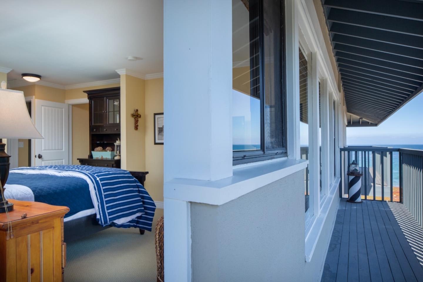 Bedroom with blue-striped bedding beside a covered balcony overlooking the ocean.