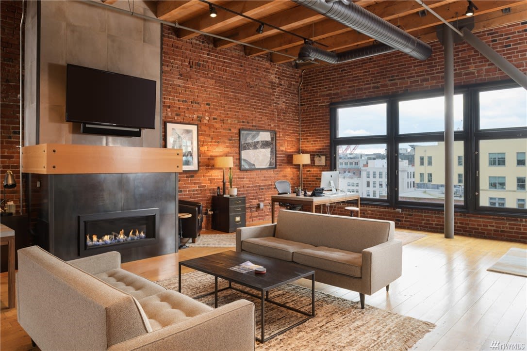 Experience high-end city living in this chic loft living room with a cozy fireplace, brick walls, and urban views.