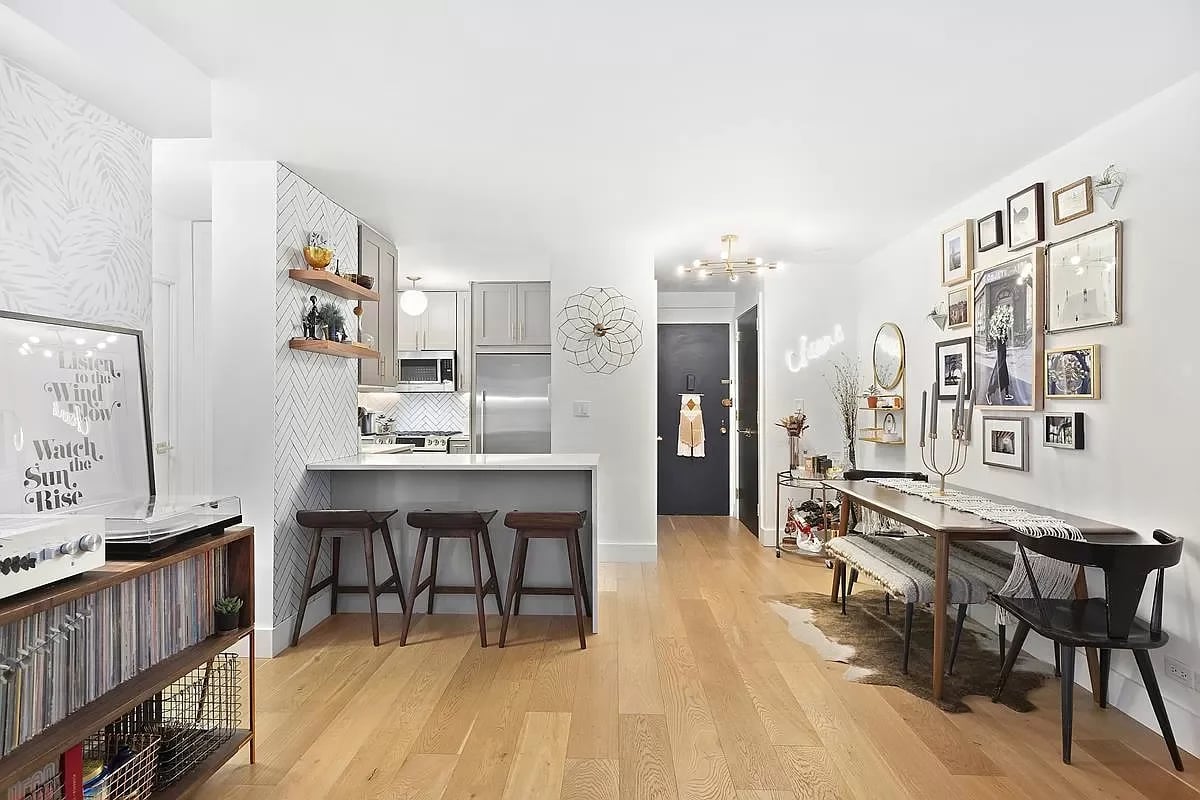 Open-plan apartment with a tiled kitchen breakfast bar, light wood floors, and a dining area beneath a gallery wall.