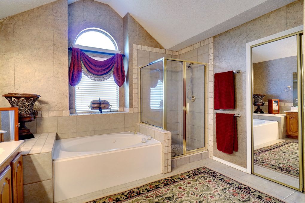 Bathroom with a built-in tub beneath an arched window and a separate glass-enclosed shower.
