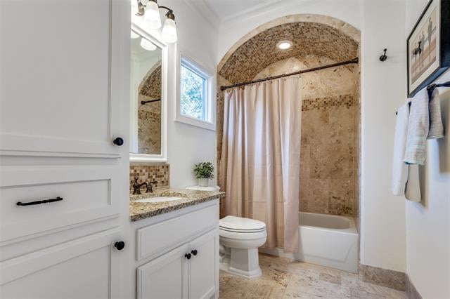 Bathroom with an arched tan-tiled tub alcove, white vanity, and toilet.