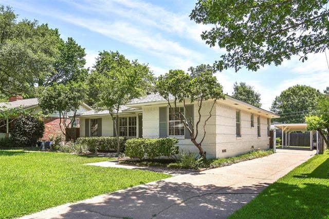 Single-story home with a green lawn, mature trees, and a driveway leading to a covered carport.
