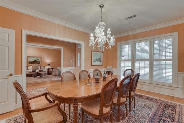 Dining room with an oval wooden table, crystal chandelier, and large windows with white blinds.