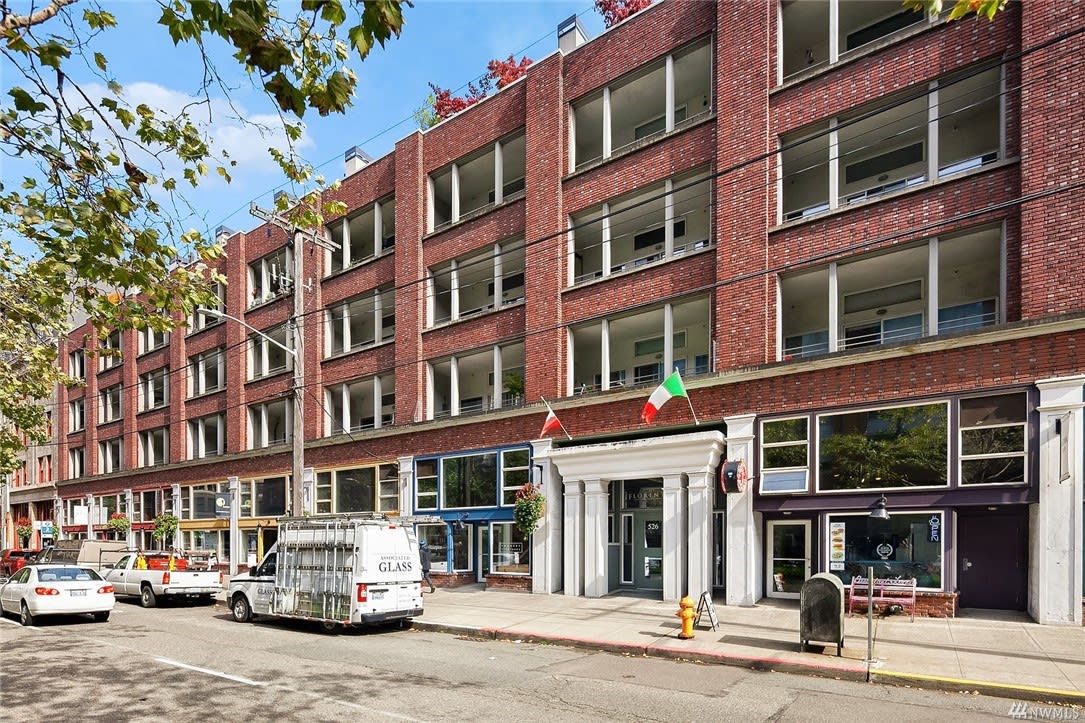 A bustling street with cars parked in front of a grand brick building.