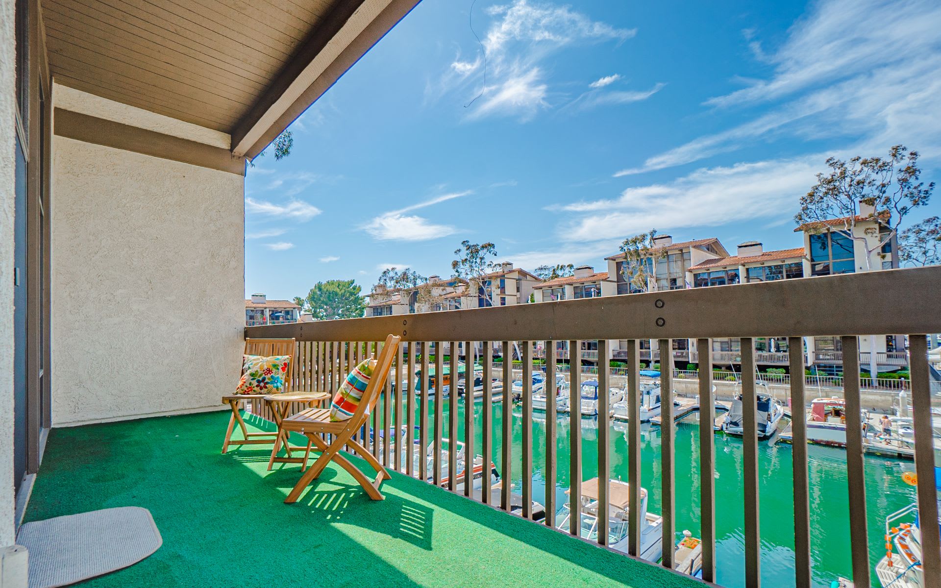 Apartment balcony with wooden chairs overlooking boats in a marina.