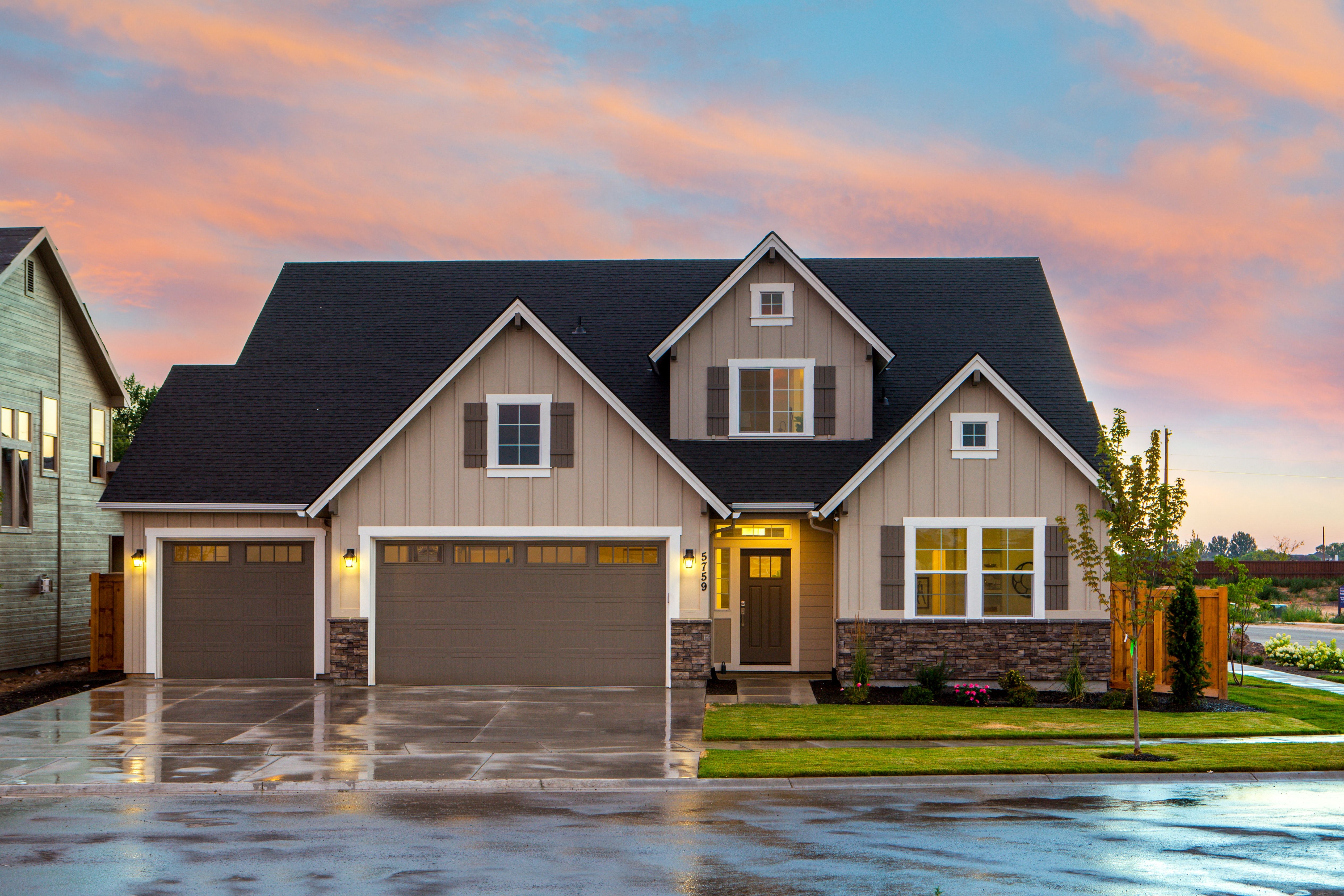 Two-story beige house with multiple gables, stone accents, and a double garage at sunset.
