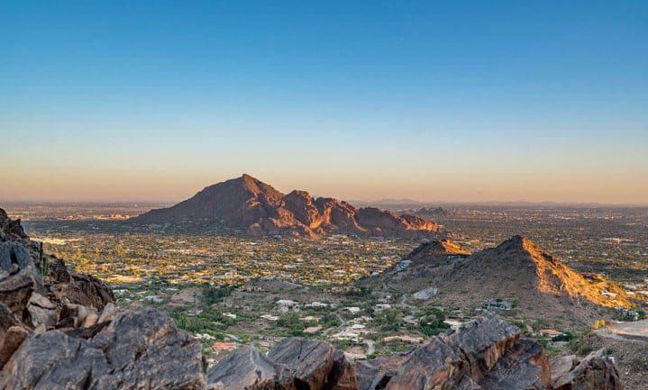 Panoramic view of a city from a mountain top, showcasing its buildings, bridges & winding river